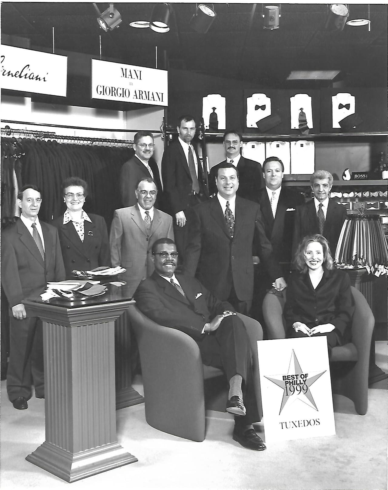 A black-and-white photo of the store’s staff posed among the suits beside a Best of Philly 1999 Tuxedos sign