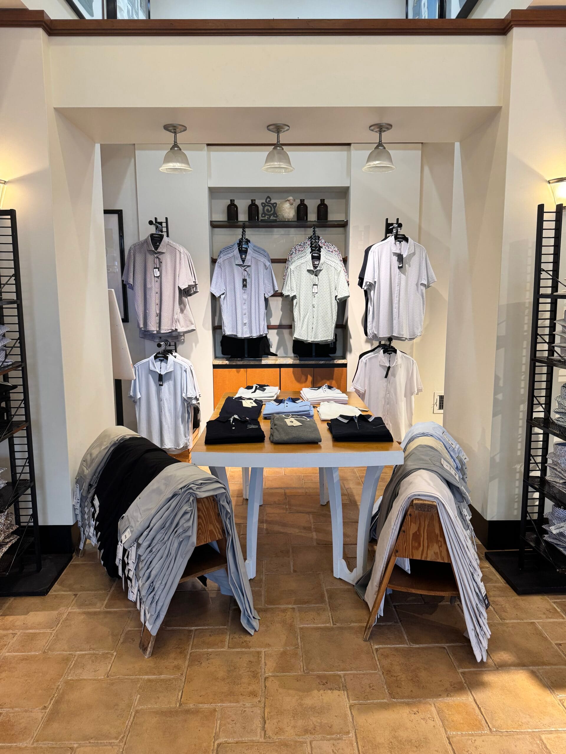 Inside the store: a table of folded sweaters and pants in front of a wall of casual shirts on display forms