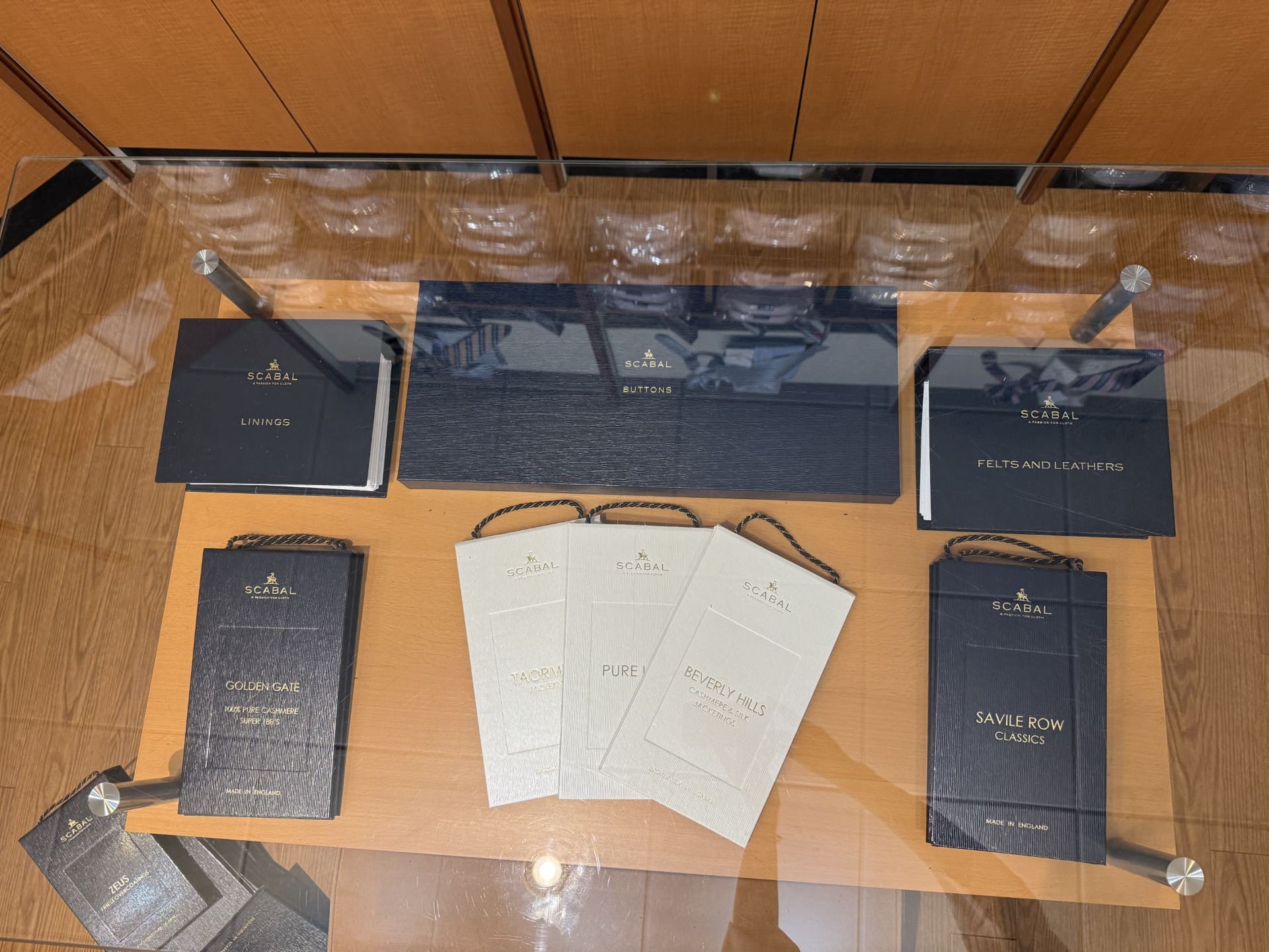 Scabal cloth books for linings, buttons and suitings laid out on a glass table