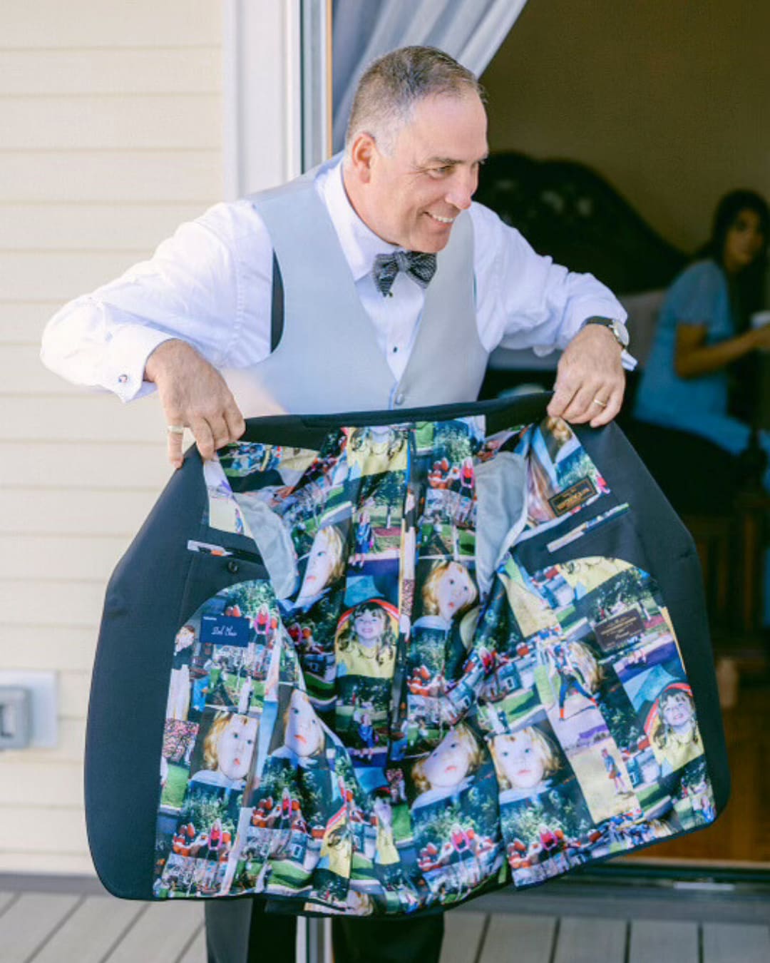 A man in a grey vest and bow tie opening his jacket to show a lining printed with family photos