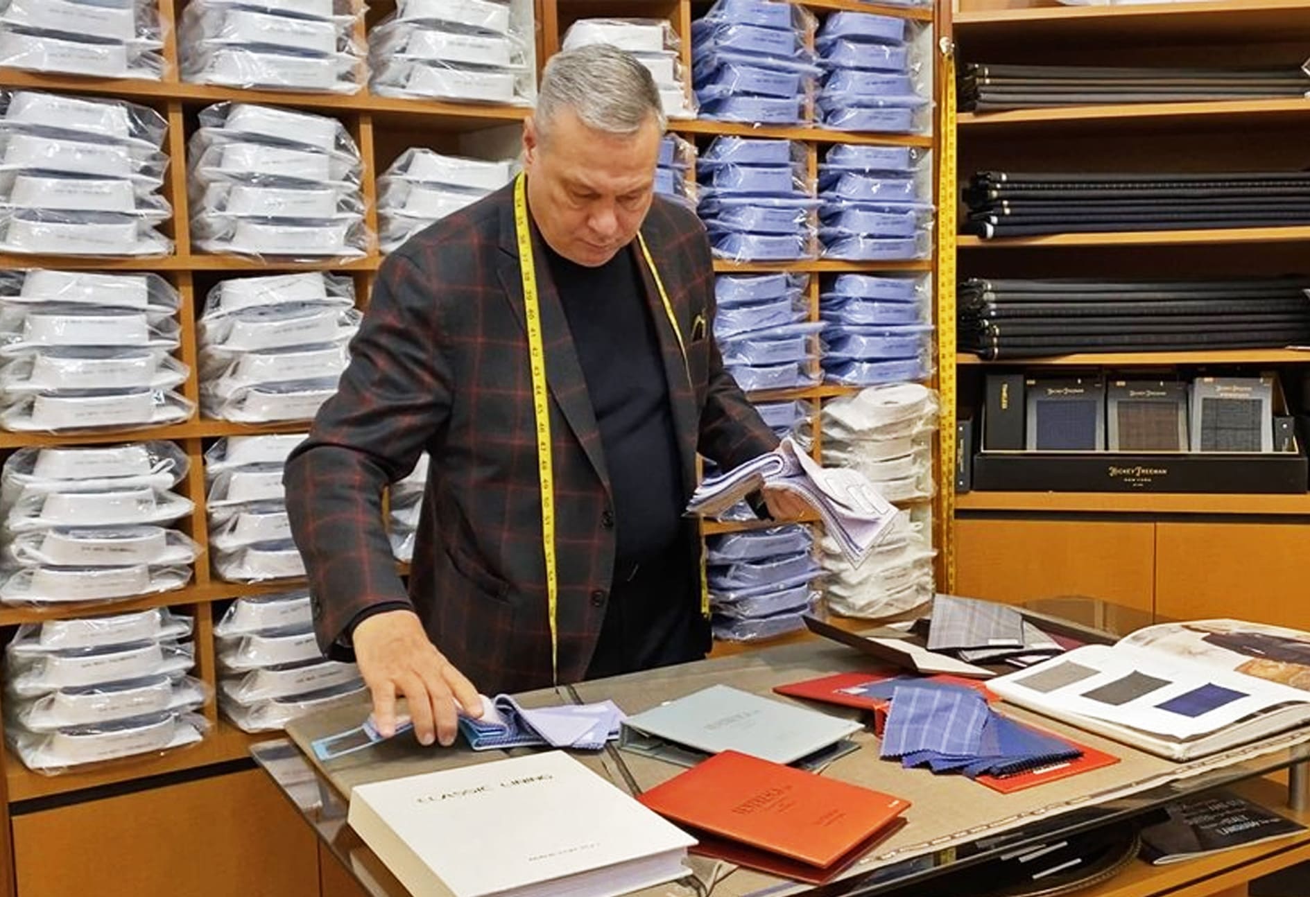 Frank Ventresca at the store’s counter, a yellow tape measure around his neck, sorting shirt fabric among the cloth books