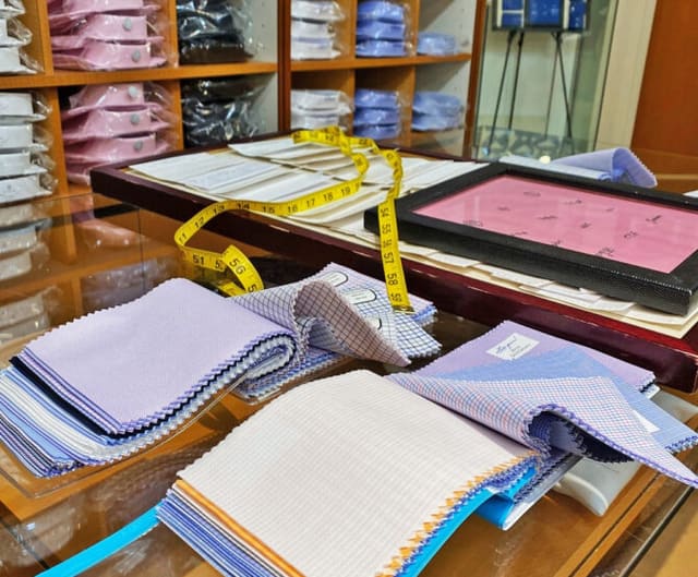 Shirting swatch books in lavender, blue and white stripes, with a yellow tape measure, on the counter