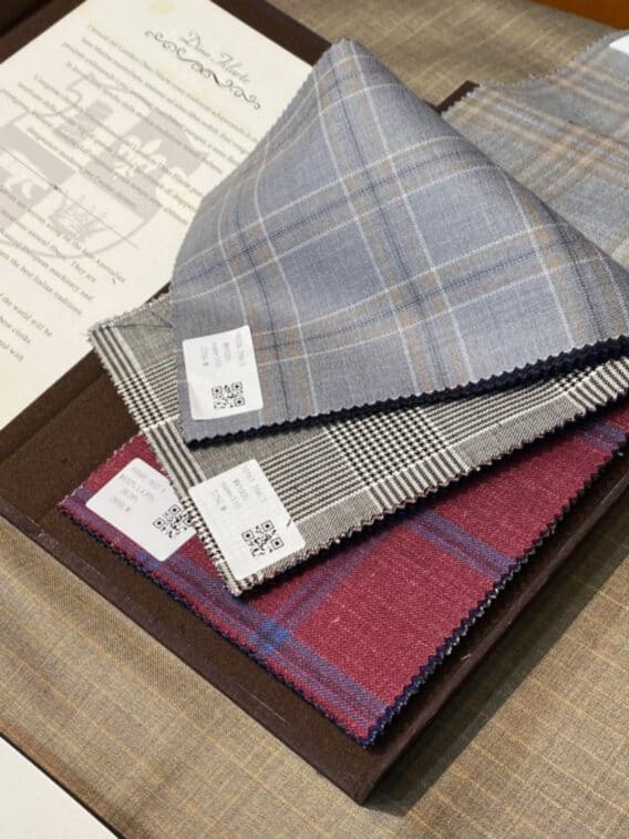 Suiting swatches in grey windowpane, glen plaid and burgundy check, fanned out on a cloth book