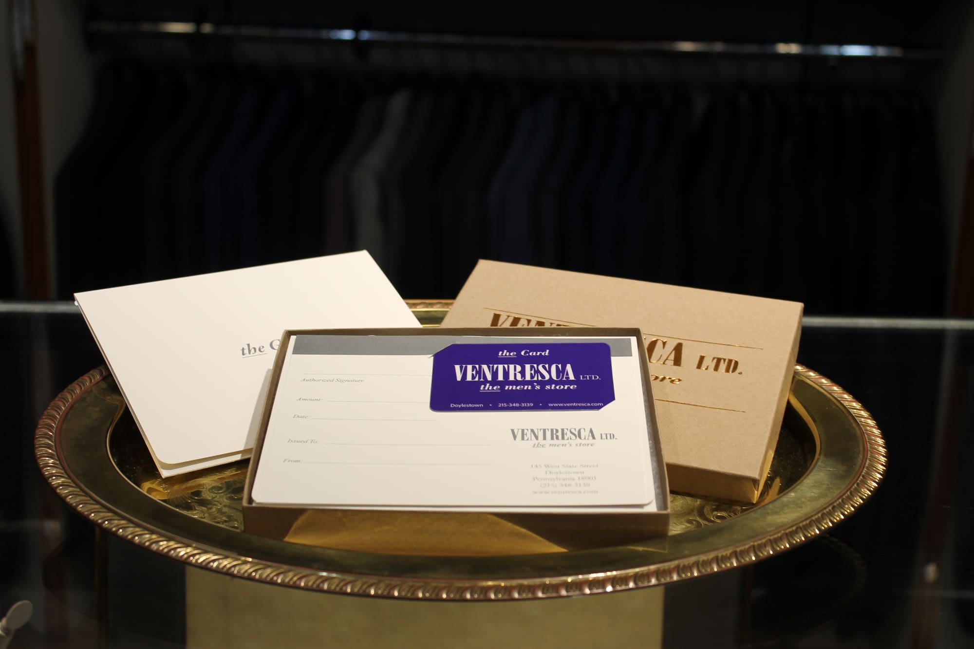 A Ventresca Ltd. gift card in its presentation box, with a cream envelope and a kraft gift box stamped in gold, on a brass tray in the store