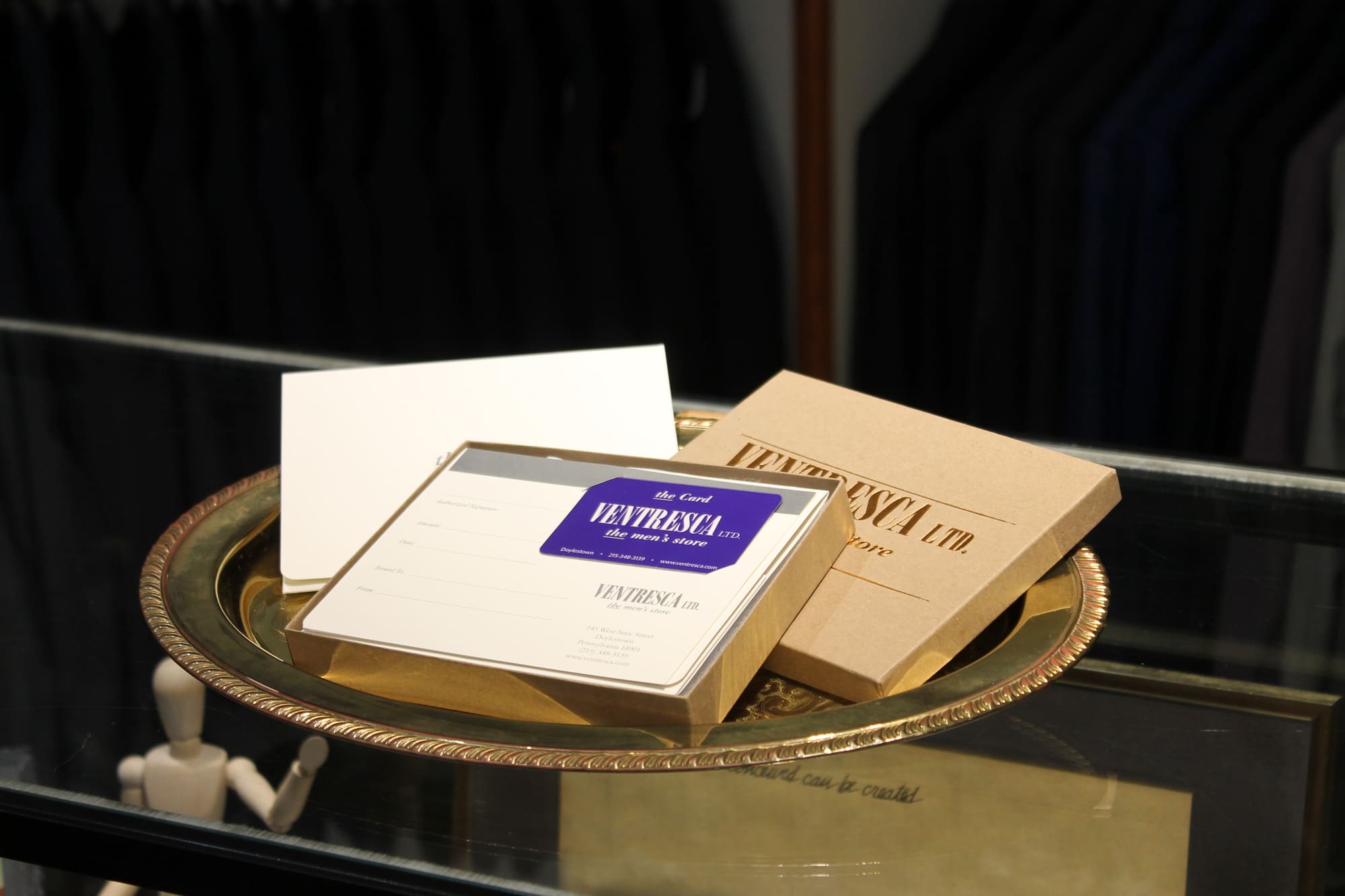 A closer look at the gift card set on its brass tray: the purple Ventresca card in its box, beside a cream envelope and the kraft gift box