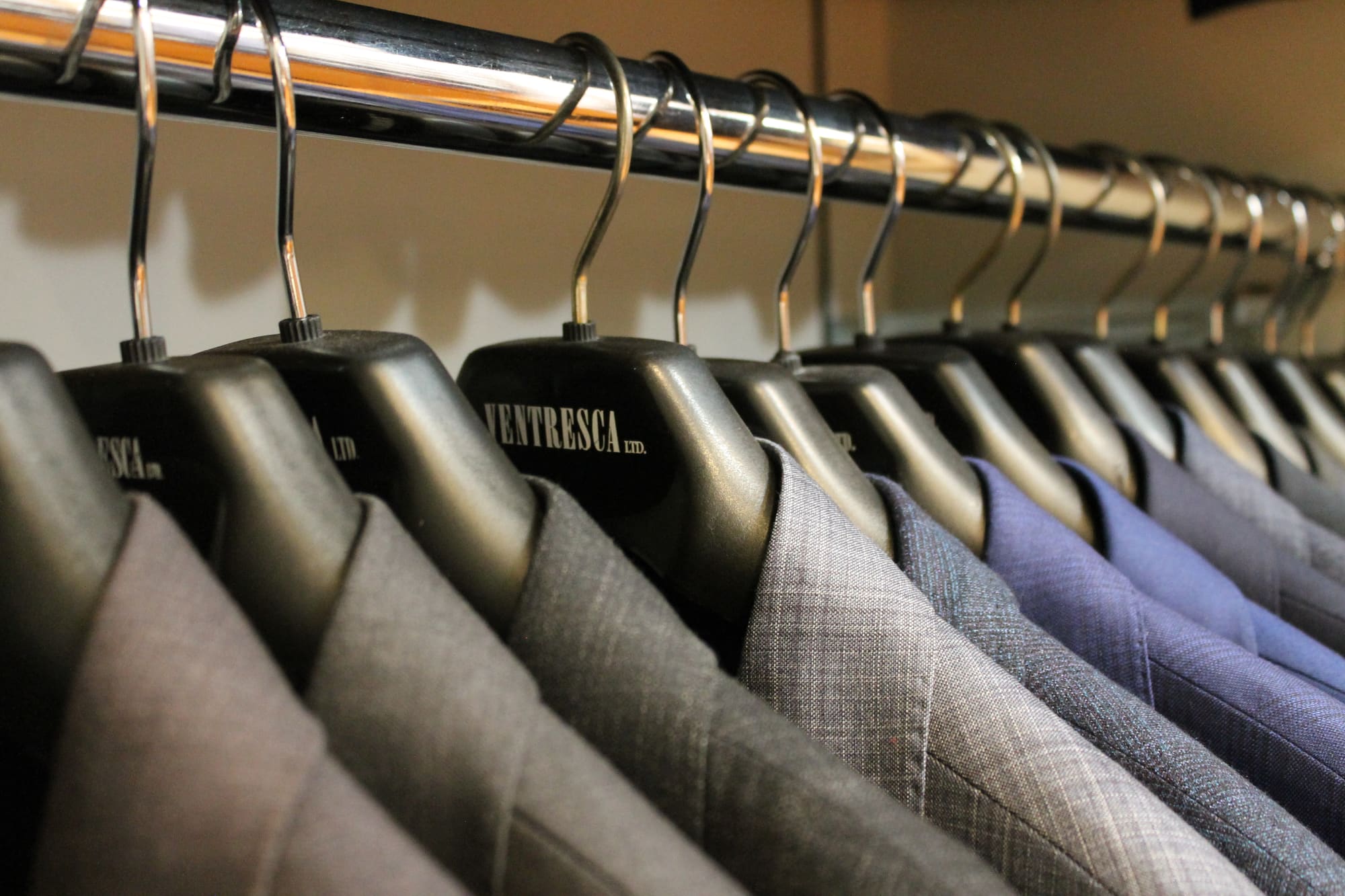 Suit jackets in grey, blue and windowpane check hanging on black Ventresca Ltd. hangers