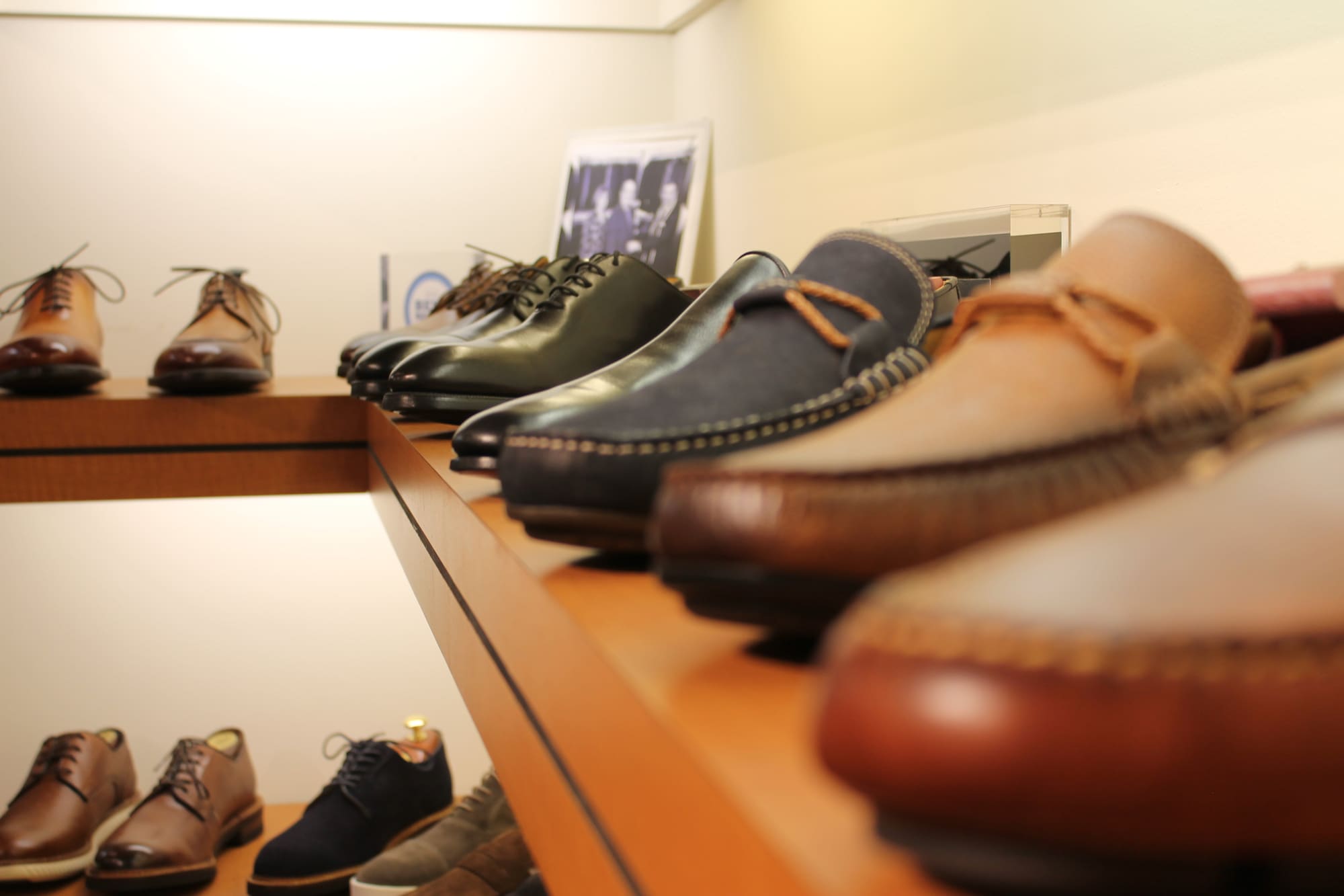 Suede and leather driving moccasins lined up along a wooden shelf, lace-ups on the shelf below