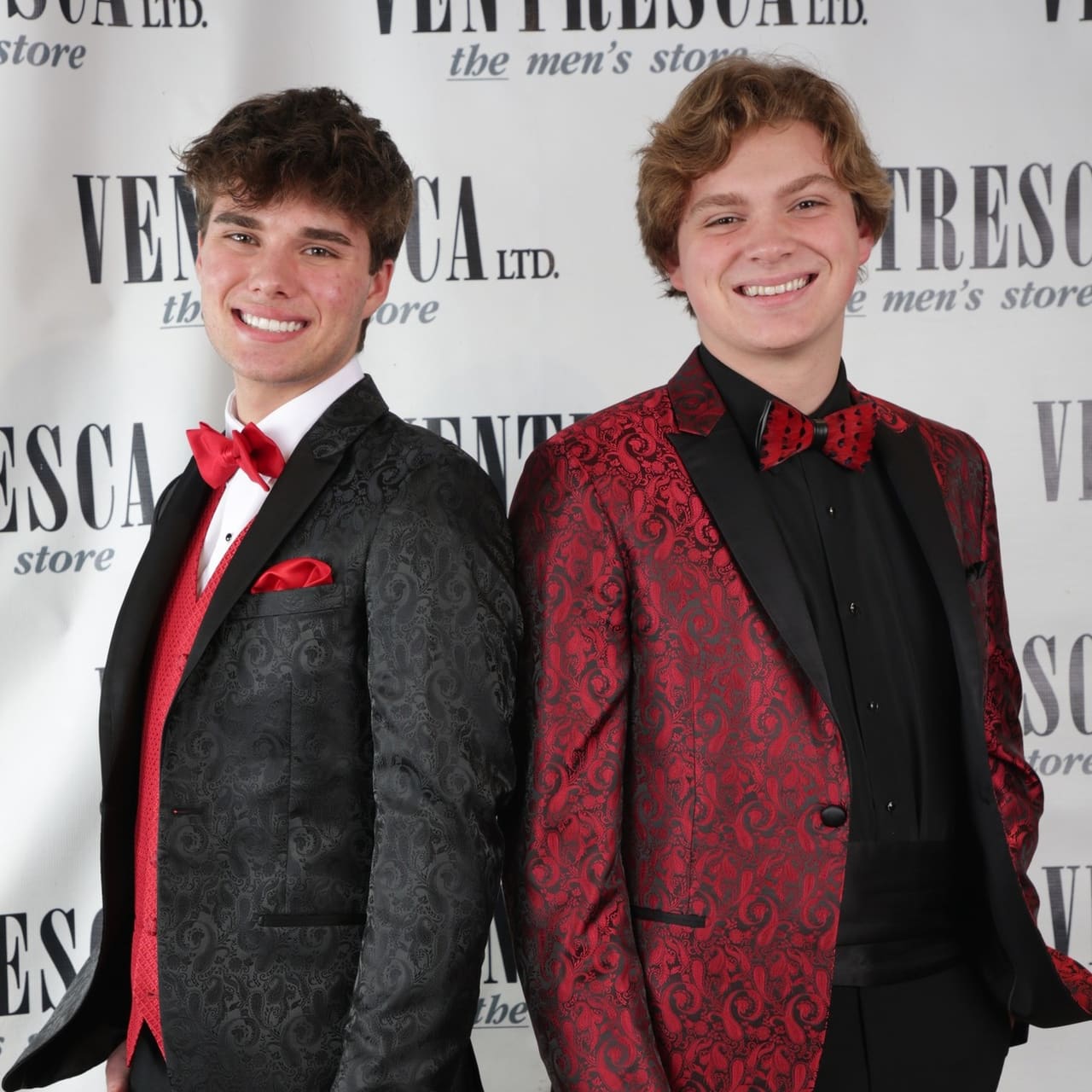Two young men in patterned black and red dinner jackets with red bow ties, dressed for prom