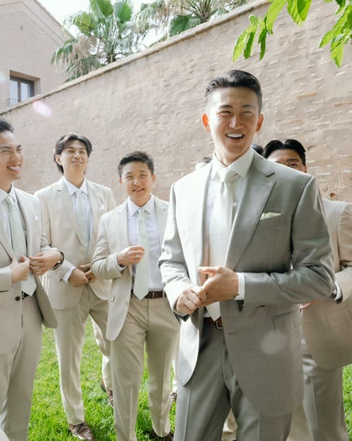 A groom in a sage suit laughing with groomsmen in tan suits